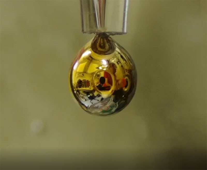 Electrons from a droplet of sodium and potassium diffuse onto a thin layer of water, turning it golden and giving it metallic properties. (Photo: Nature/Philip E Mason)
